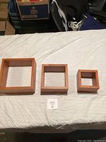 Three wooden square shelves placed on a white surface showing the front side of the frames.