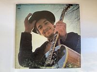 Front cover of the Bob Dylan Nashville Skyline vinyl record album showing artist holding guitar and tipping hat.