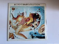 Front of the vintage Dire Straits vinyl record album 'Alchemy Dire Straits Live' featuring surreal cover artwork with distorted figures and musical instrument imagery.