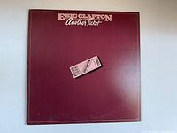 Front cover of Eric Clapton "Another Ticket" vinyl record album showing maroon background with ticket graphic and title text.
