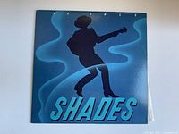Front cover of the J.J. Cale Shades vinyl record album featuring a silhouette of a guitarist and album title in blue tones.
