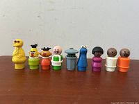 All 9 Sesame Street figures standing in a row on a wooden surface.