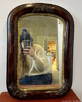Front view of Victorian antique wall mirror showing oval shape, dark wood frame with raised harvest fruit decorations, and mirror surface with wear.