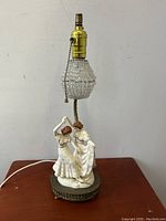 Photo of ceramic Art Deco flapper ladies table lamp showing detailed figures and beaded glass shade, lamp is unlit.