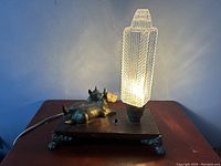 Lit view of the Art Deco lamp showing the textured glass shade and the Scotty dog figure on the base with claw feet.