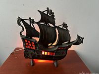 Front view of illuminated cast iron galleon ship table lamp showing glowing windows and original cord