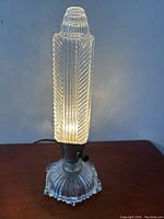 Clear glass Art Deco style skyscraper tower lamp lit, showing ribbed vertical texture and illuminated warm light.