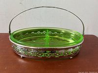 Oval Vaseline uranium glass bowl set in silvered metal holder with handle, resting on table.