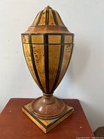 Front view of burled wood urn showing black vertical stripes and square base, no finial on lid