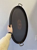 Side view showing tray held upright with metal handles visible and oval shape.