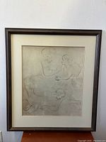 Framed abstract nude art print leaning against a white wall on a wooden surface, showing the full artwork and frame.