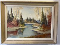 Front view of large oil painting showing autumn scenery with river and cabin, framed.
