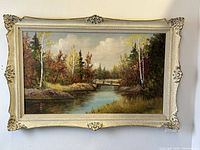 Frontal view of the large scenic oil painting in cream decorative wood frame hung on a white wall.