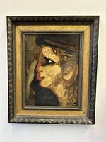 Framed oil painting showing a profile portrait of a figure in modernist style with signature visible.