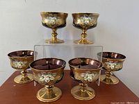 Six Bohemian royal purple stemmed sherbet compote bowls with gilt stems and white floral enamel decoration arranged with some elevated.