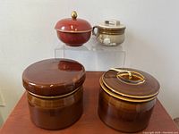 Front view of four ceramic lidded pots stacked on clear acrylic stands showing size variations and details.