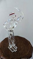 Front and slight left side view of the clear crystal flamenco dancer figurine showing raised right arm, tilted hat with red band, and bent left arm.