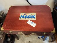 Closed view of one wooden case showing the reddish-brown wood, metal corner protectors, leather handle, and "MAGIC WINDOW" sticker on top.
