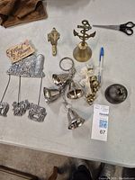 Lot arranged on a white surface showing multiple bells and metal decorative pieces, including animal spike figures, brass bell with anchor handle, small handbells, and a round item.