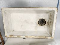 Top-down view of rectangular cast iron sink showing drain area with rust and worn white enamel.