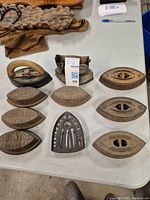 Top-down photo of nine vintage cast iron irons and one cast iron stand on table showing various sizes and shapes.