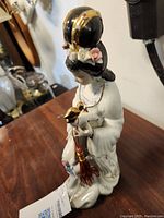 Porcelain figurine showing full figure of woman with bird and broom accessory on wooden surface.