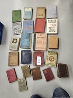Overview of a crate spread out with 21 assorted vintage and classic books in different colors and conditions on a grey floor.
