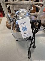 Front and side view of the chrome General Electric electric teapot with attached power cord and black handle.