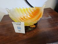 Yellow and orange scalloped glass bowl on cast iron trivet on wooden surface.