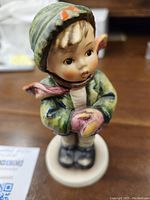 Close-up image showing the figurine of a young child wearing a green coat, striped scarf, and mittens, standing on a base.
