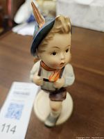 Porcelain figurine of a young school boy, showing detailed hand-painted features and outfit with blue hat and orange scarf.