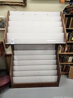 Full front view of the wooden magazine rack showing white angled shelves and dark wood sides.