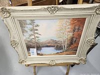 Front view of framed landscape oil painting featuring lake, trees, and mountains in autumn colors, signed T. Laaksonen.