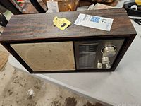 Front view of vintage Lloyds radio showing wood grain finish, cloth speaker cover, frequency display, and three chrome knobs.