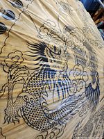 Close-up of umbrella fabric showing large black dragon design with flames and detailed scales on beige background.