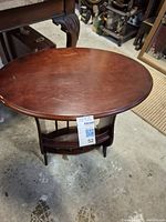 Oval wooden hall table with a lower shelf and visible wear marks on the top surface.
