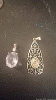 Two .925 sterling silver pendants, one with a rose quartz stone and diamond accent, the other a vintage abalone shell pendant with filigree design, photographed on a dark surface.