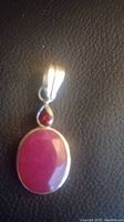 Front view of pendant showing two ruby stones set in sterling silver, on a black textured background.