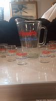Photo showing Hamm's Beer pitcher and six small matching vintage Hamm's beer glasses with gold rims on a white surface.