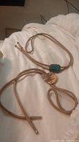 Photo showing two vintage bolo ties with tan braided ropes, one with turquoise stone set in silver and one with circular agate stone.