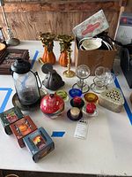 Wide view of all candlestick holders, candles, wax melts, cast iron burner, box with candle warmer, and other candle accessories on table in garage setting.