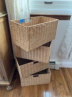 Four stacked woven rectangular baskets with handle cutouts in natural fiber.
