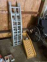 Photo showing two aluminum vehicle ramps and one yellow plastic truck bed ramp on a garage floor.