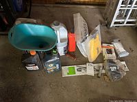 View of chainsaw liquids, green funnel, orange container, chainsaw chain in packaging, and manuals on garage floor.