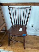 Front view of the vintage wooden chair showing the spindle backrest and shaped seat with scratches.