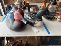 Pair of carved wooden decoy ducks displayed on a table with price tags showing. The ducks are detailed and signed, in gently used condition with some visible scratches.