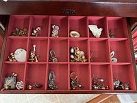 Top down view of divided jewelry box with compartments containing multiple pairs of earrings and pins of vintage and costume jewelry style.