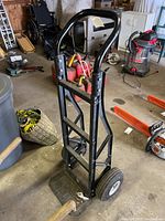 Front angle view of the black plastic frame hand truck showing curved handle and wheels.