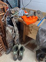 Full view of waders, boots, hats, and gloves on basement floor and wooden desk.