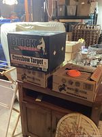 Boxed Block Fusion crossbow target and two White Flyer clay target boxes stacked on a wooden dresser in basement.